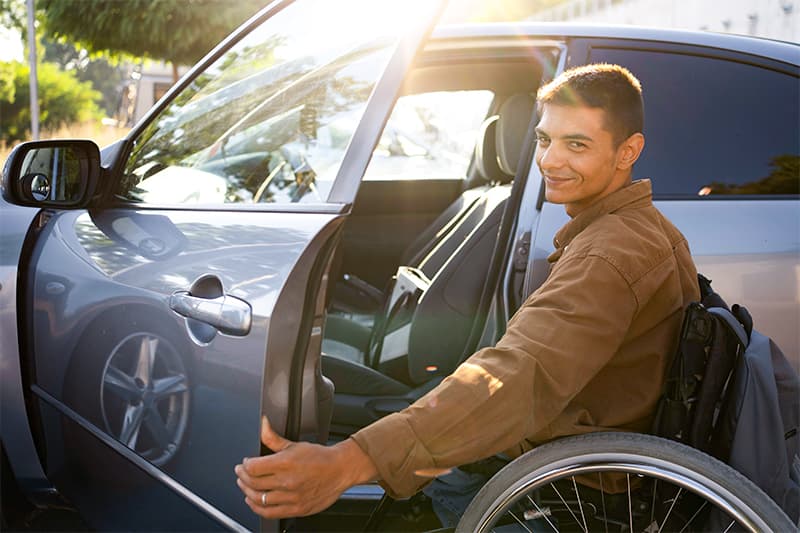 manual wheelchair user getting into driver's seat of car.